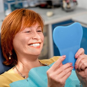Woman examining her smile in handheld mirror
