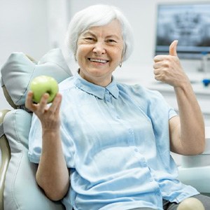 Woman holding an apple and giving a thumb up from the patient’s chair