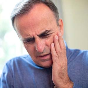 Man with hand on face experiencing pain after dental implant surgery