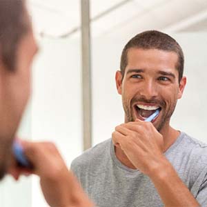 Man smiling while brushing teeth in mirror