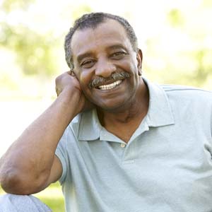 Man smiling outside in grey polo after dental implant tooth replacement