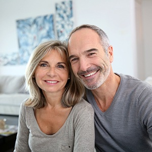 happy couple with dental implants in Haverhill sitting on a couch 
