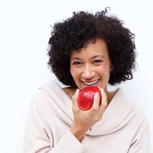 Woman with dental implants biting into a red apple