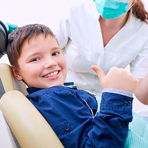 Child in dental chair giving thumbs up
