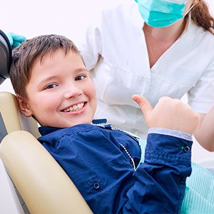 Child in dental chair giving thumbs up during children's dentistry visit