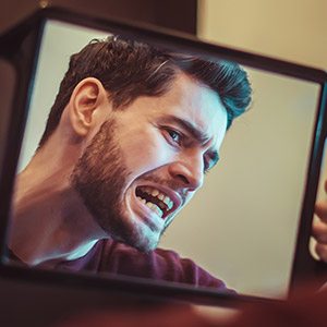 Man in need of restorative dentistry looking at damaged smile in the mirror