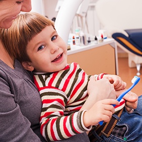 Mother holding child in lap at dental office for family preventive dentistry visit