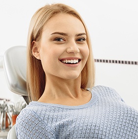 Woman in dental chair smiling after replacing missing teeth