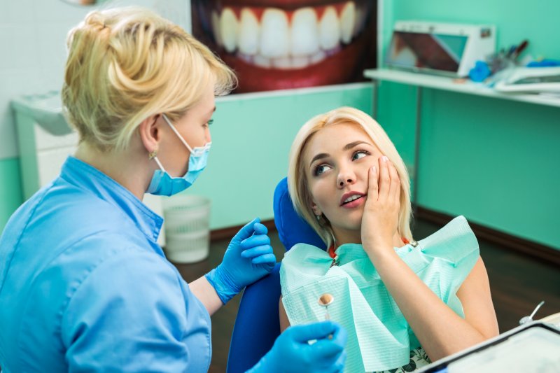 a female patient holding her cheek in a pain at the dentist office