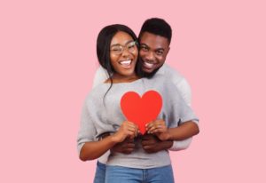 young couple in gray sweaters holding red paper heart